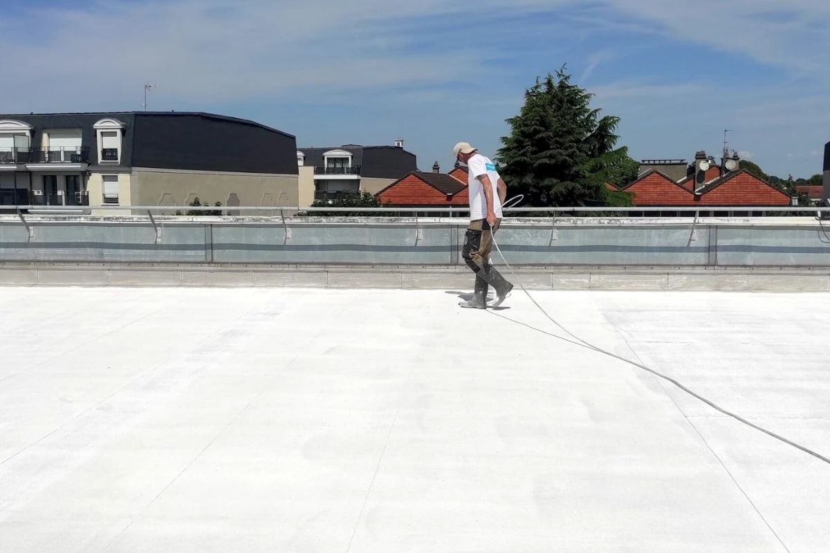 Technicien Cooltech appliquant la peinture réflective PRIMATHERM sur une toiture plate