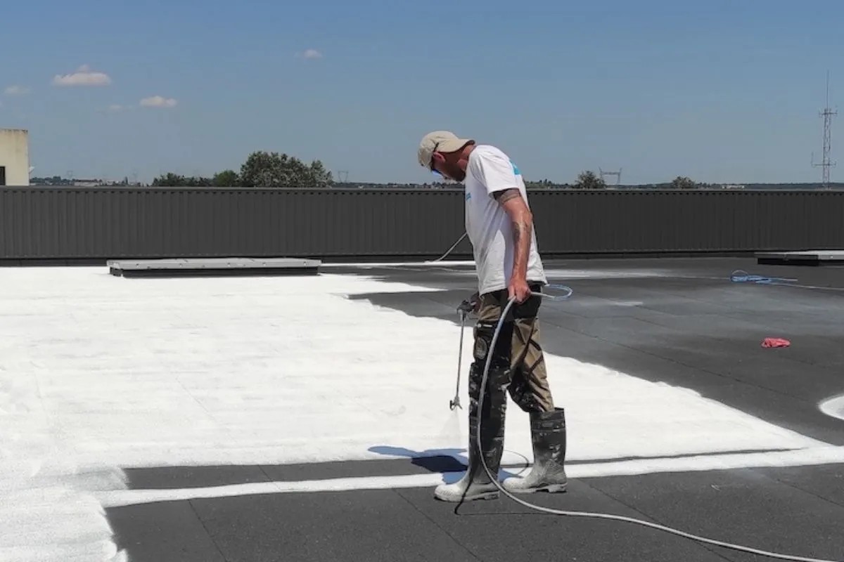 Technicien Cooltech appliquant la peinture réflective PRIMATHERM® au pistolet sur un toit plat de bâtiment public.