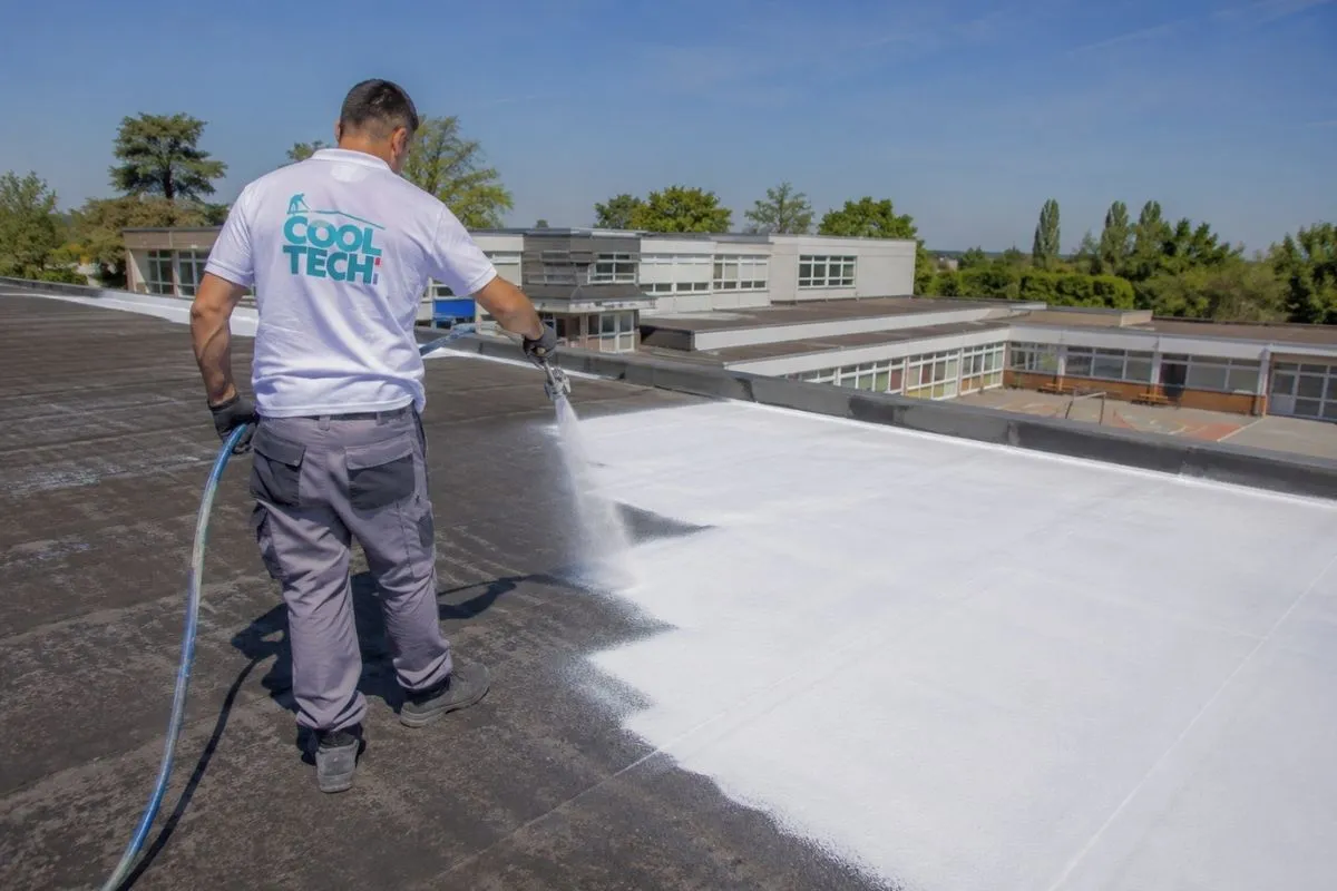 Technicien Cooltech appliquant la peinture réflective PRIMATHERM® au pistolet sur un toit plat de bâtiment public.