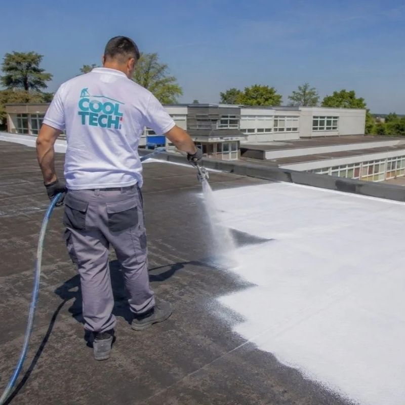Technicien Cooltech appliquant la peinture réflective PRIMATHERM® au pistolet sur un toit plat de bâtiment public
