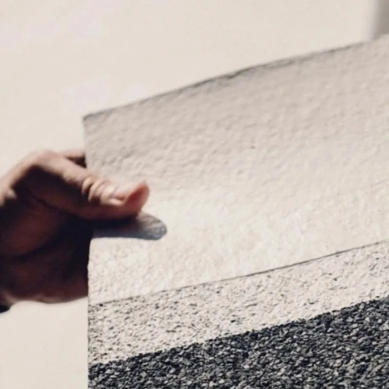 Échantillon d'un revêtement pour toiture montrant le contraste entre la surface blanche réfléchissante et le support sombre d'origine