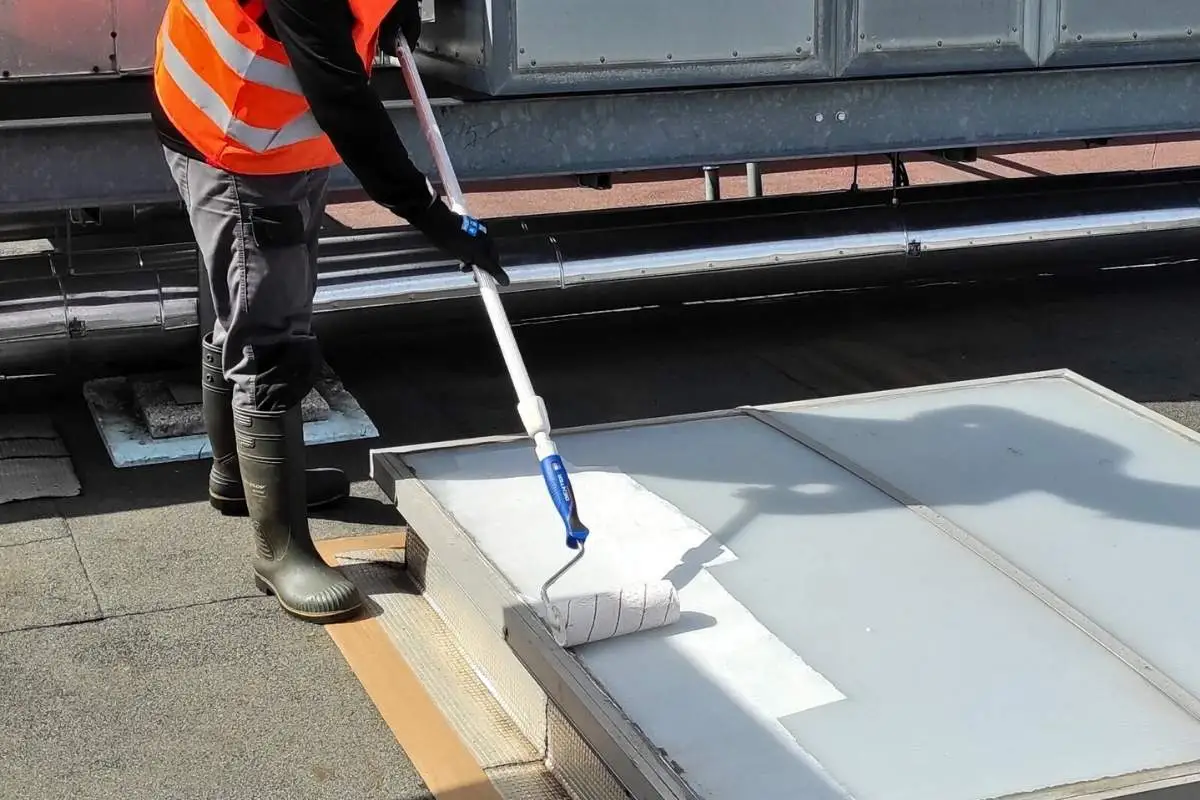 Technicien Cooltech appliquant la peinture réflective au rouleau sur un relevé de toiture