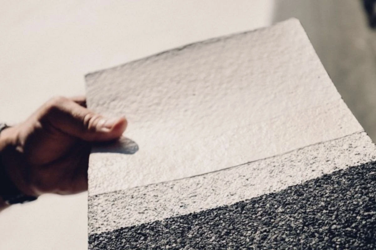 Échantillon d'un revêtement pour toiture montrant le contraste entre la surface blanche réfléchissante et le support sombre d'origine
